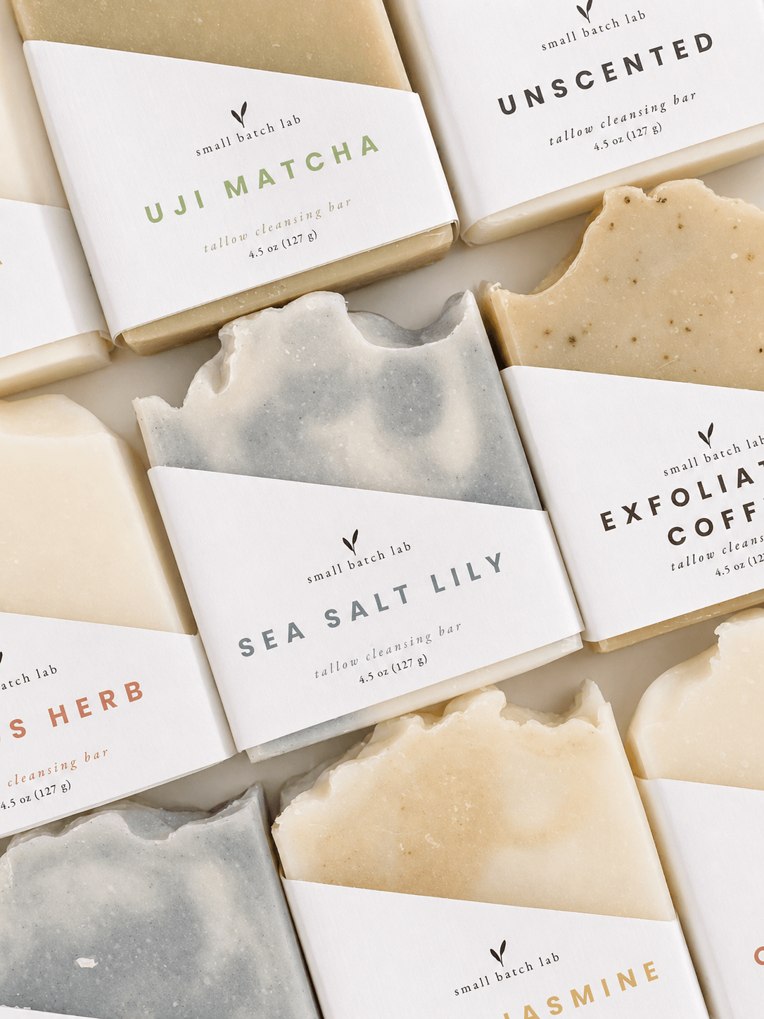 artisan grass-fed beef tallow bars of soap in earthy tones are arranged on a foamy, wet marble surface. Natural sponges and smooth stones add an organic, calming feel.