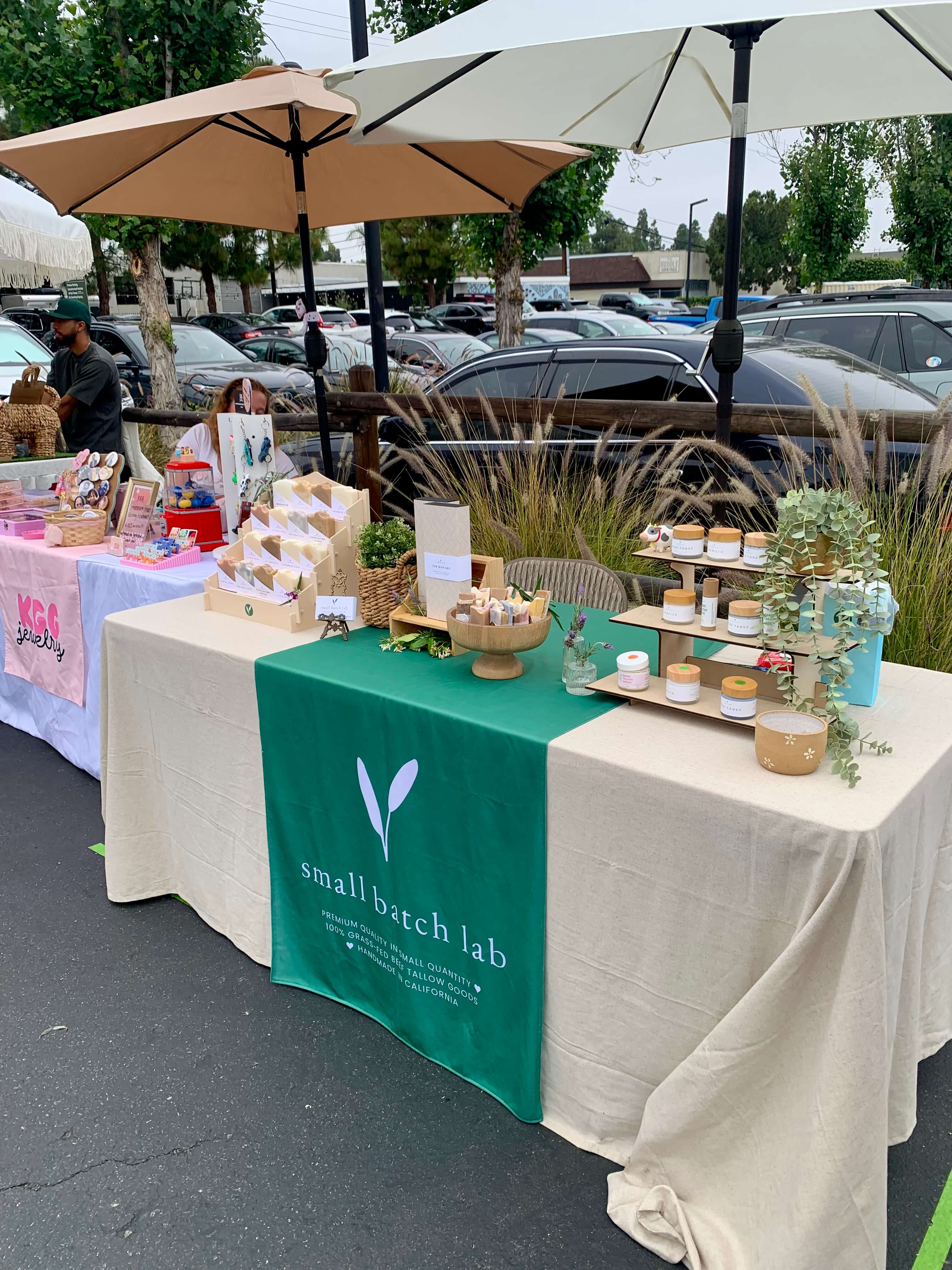 Outdoor market stall with 'Small Batch Lab' branding, featuring products under umbrellas.